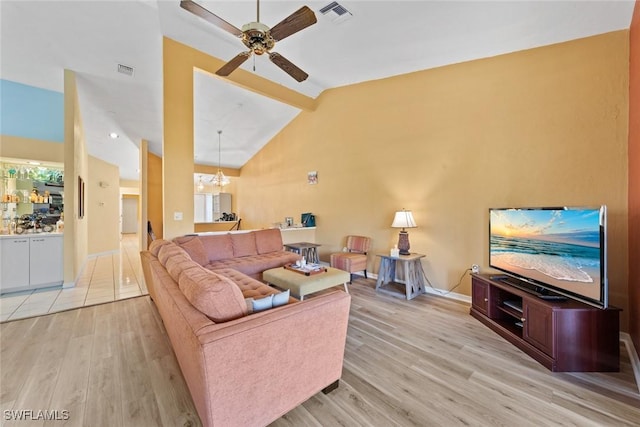 living area featuring ceiling fan with notable chandelier, high vaulted ceiling, light wood finished floors, and visible vents