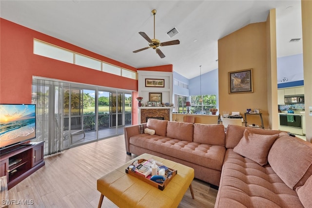 living room with a brick fireplace, high vaulted ceiling, ceiling fan, and light hardwood / wood-style flooring