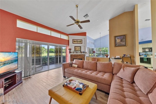 living area with high vaulted ceiling, a fireplace, visible vents, and a ceiling fan