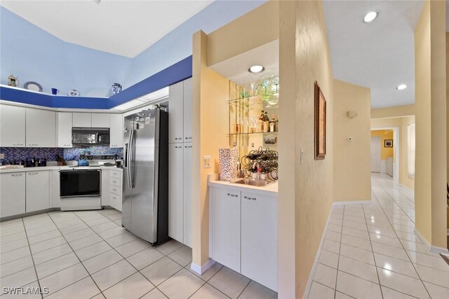 kitchen with stainless steel refrigerator with ice dispenser, light tile patterned floors, white cabinets, electric stove, and backsplash