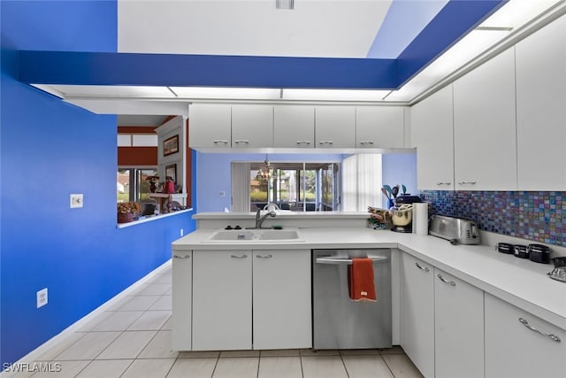 kitchen with sink, light tile patterned floors, stainless steel dishwasher, kitchen peninsula, and white cabinets