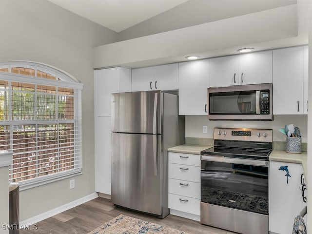 kitchen with stainless steel appliances, white cabinetry, vaulted ceiling, and light hardwood / wood-style floors