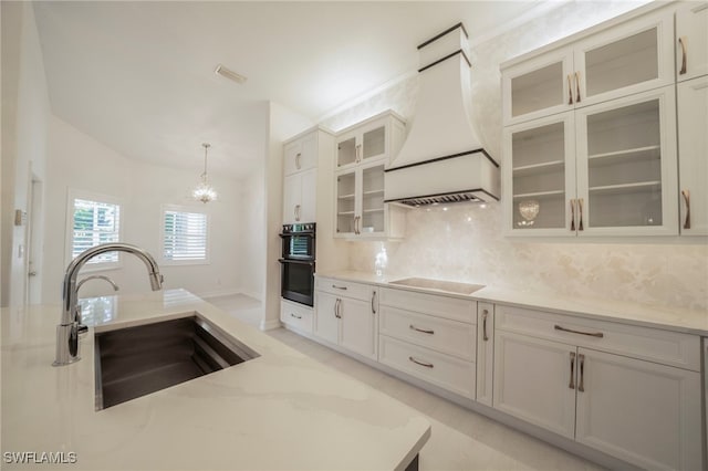 kitchen featuring decorative backsplash, light stone counters, black appliances, premium range hood, and sink