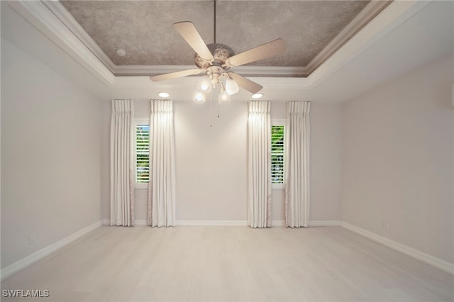 empty room featuring ceiling fan, a raised ceiling, and plenty of natural light