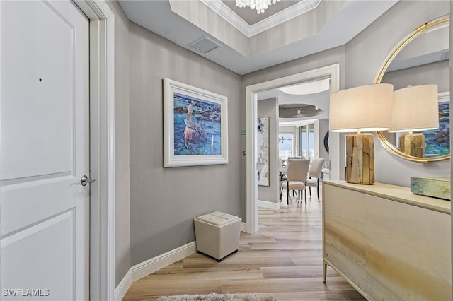 hall featuring a tray ceiling, ornamental molding, light wood-type flooring, and an inviting chandelier