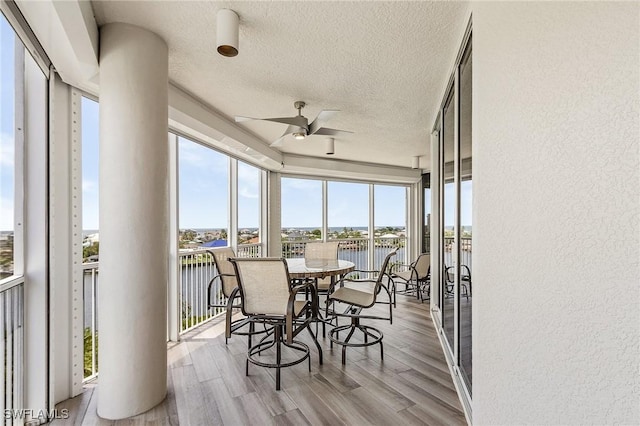 sunroom with ceiling fan and a water view