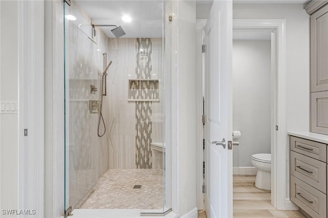 bathroom featuring toilet, a tile shower, and wood-type flooring