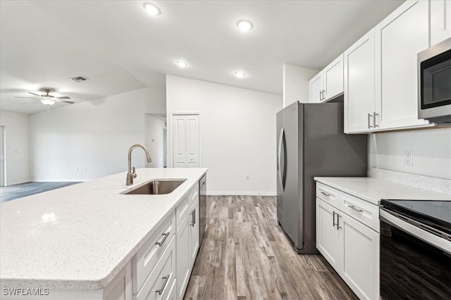 kitchen with sink, white cabinetry, stainless steel appliances, a center island with sink, and vaulted ceiling