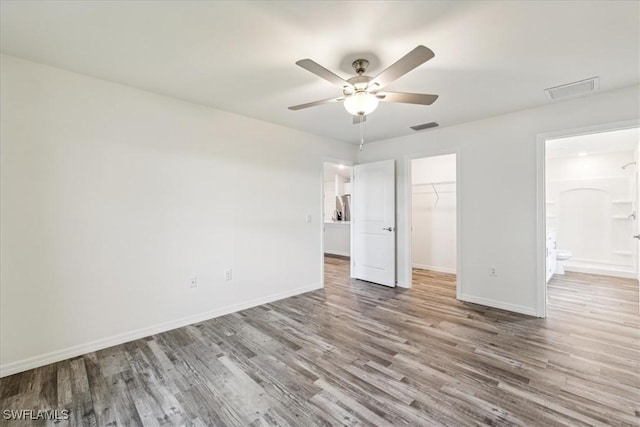 unfurnished bedroom featuring ensuite bath, ceiling fan, wood-type flooring, a walk in closet, and a closet