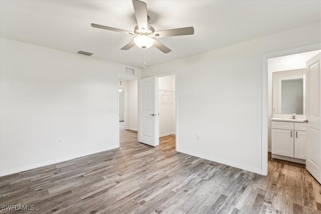 unfurnished bedroom with sink, light hardwood / wood-style flooring, ceiling fan, a walk in closet, and a closet