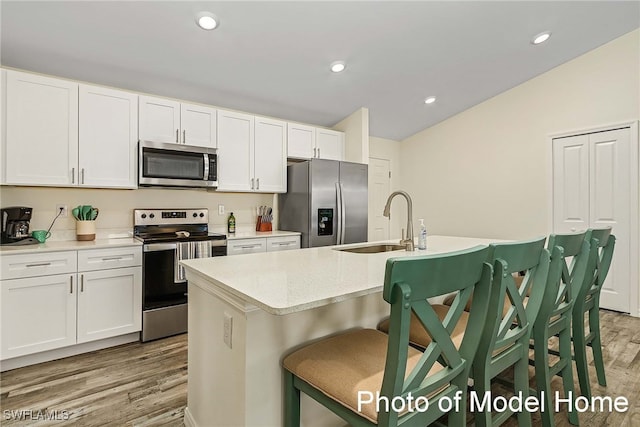 kitchen with stainless steel appliances, a kitchen island with sink, a breakfast bar area, and white cabinets