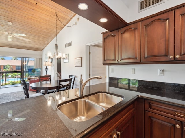 kitchen featuring dark stone countertops, ceiling fan with notable chandelier, hanging light fixtures, vaulted ceiling, and sink