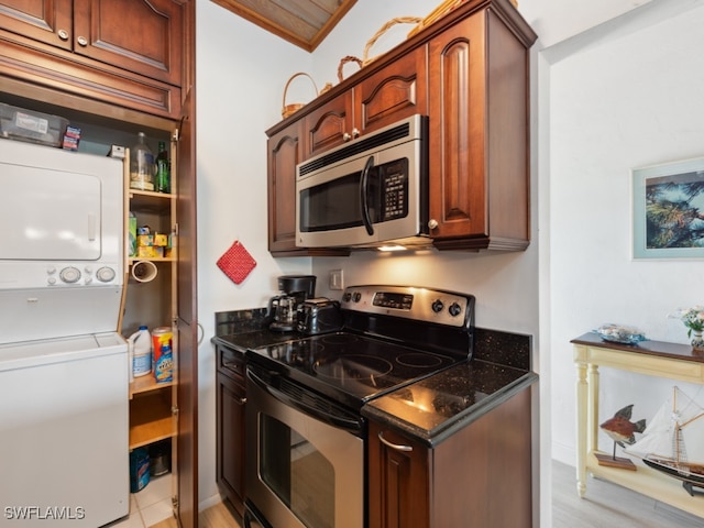 kitchen featuring stacked washer and clothes dryer, dark stone counters, and stainless steel appliances