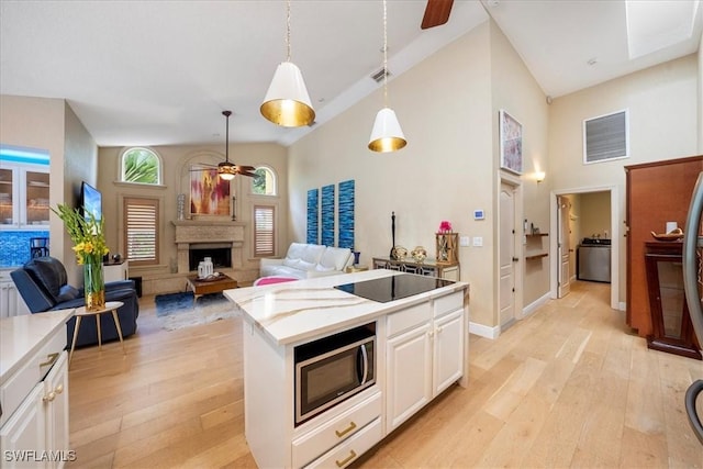 kitchen with light wood-type flooring, stainless steel microwave, white cabinets, a center island, and hanging light fixtures