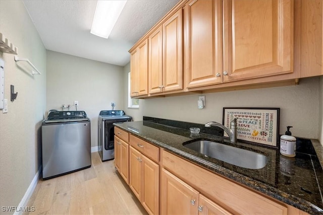 laundry room with cabinets, washing machine and dryer, sink, and light hardwood / wood-style flooring