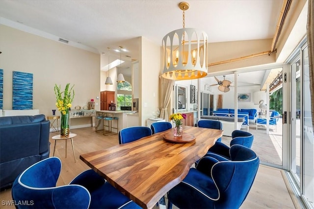 dining room featuring a wealth of natural light, light hardwood / wood-style flooring, ceiling fan with notable chandelier, and vaulted ceiling