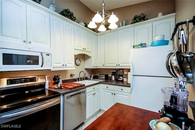 kitchen with white cabinets, dark countertops, a sink, stainless steel appliances, and a notable chandelier