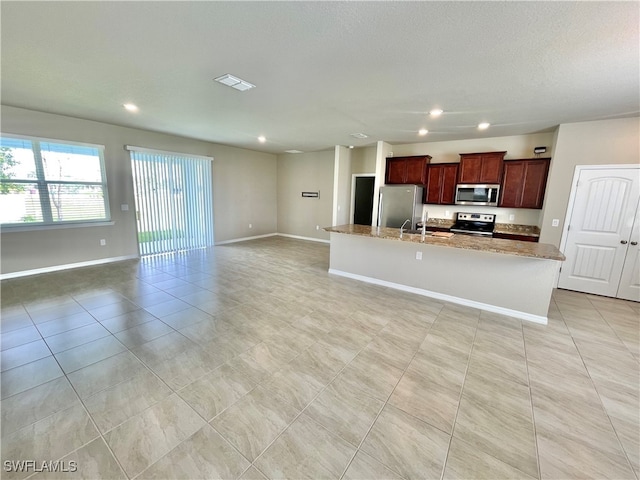 kitchen featuring light tile patterned flooring, light stone counters, stainless steel appliances, and a kitchen island with sink