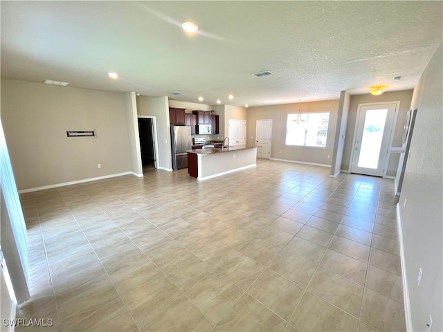 unfurnished living room featuring light tile patterned flooring, a notable chandelier, sink, and a textured ceiling