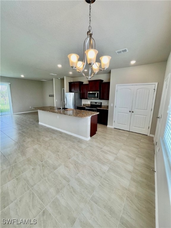 kitchen featuring a chandelier, light tile patterned floors, an island with sink, appliances with stainless steel finishes, and stone countertops