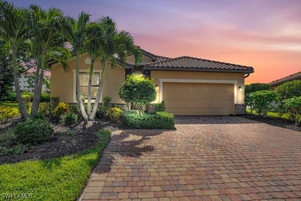 view of front of property with an attached garage, a tile roof, decorative driveway, and stucco siding