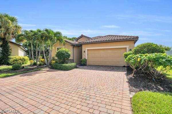 mediterranean / spanish house with a garage, a tiled roof, decorative driveway, and stucco siding