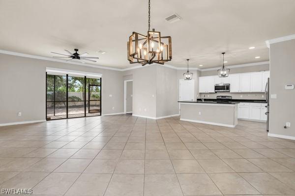 unfurnished living room featuring ceiling fan with notable chandelier, light tile patterned floors, and ornamental molding