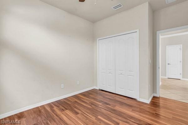 unfurnished bedroom featuring ceiling fan, wood finished floors, visible vents, baseboards, and a closet