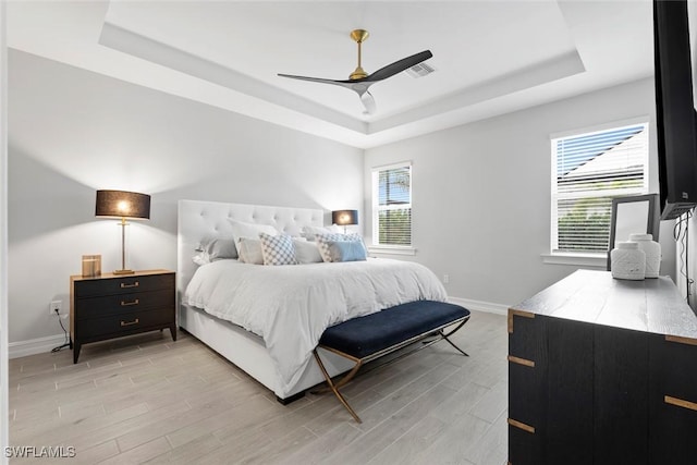 bedroom featuring visible vents, a tray ceiling, light wood-style flooring, and baseboards