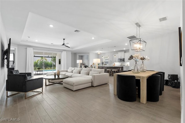 living room featuring a tray ceiling, recessed lighting, visible vents, and light wood-style floors