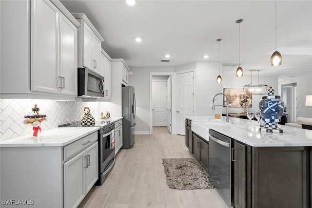 kitchen with hanging light fixtures, decorative backsplash, appliances with stainless steel finishes, a sink, and an island with sink