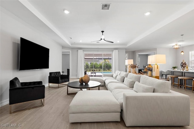 living area featuring light wood-style floors, baseboards, visible vents, and a raised ceiling