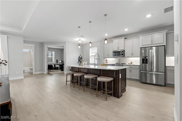 kitchen featuring stainless steel appliances, light countertops, an island with sink, a kitchen bar, and pendant lighting