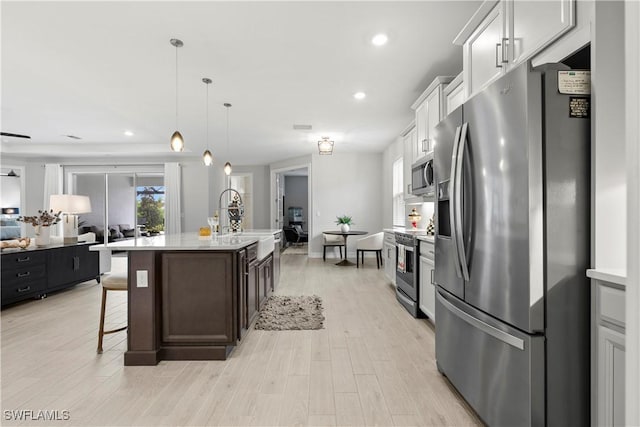 kitchen with a kitchen island with sink, stainless steel appliances, a breakfast bar, white cabinetry, and light countertops