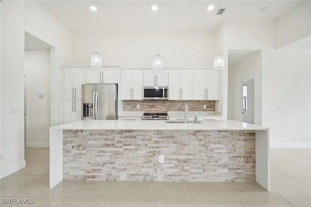 kitchen featuring tasteful backsplash, appliances with stainless steel finishes, a kitchen island with sink, light tile patterned floors, and sink