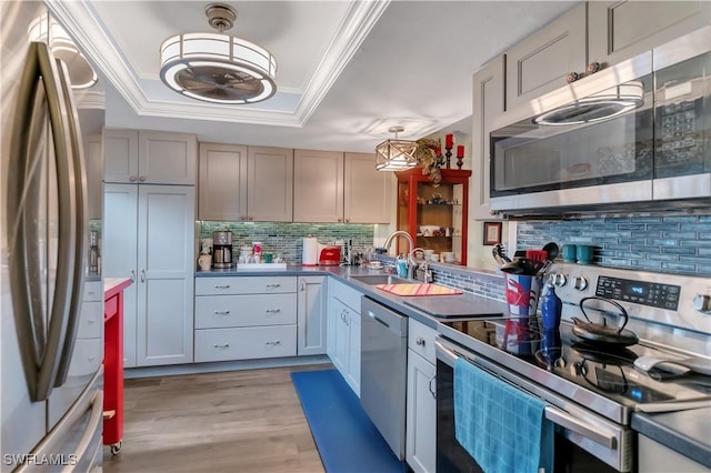 kitchen with appliances with stainless steel finishes, light wood-type flooring, tasteful backsplash, a raised ceiling, and sink