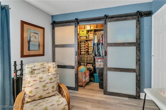 sitting room featuring a barn door, light wood-type flooring, and a textured ceiling