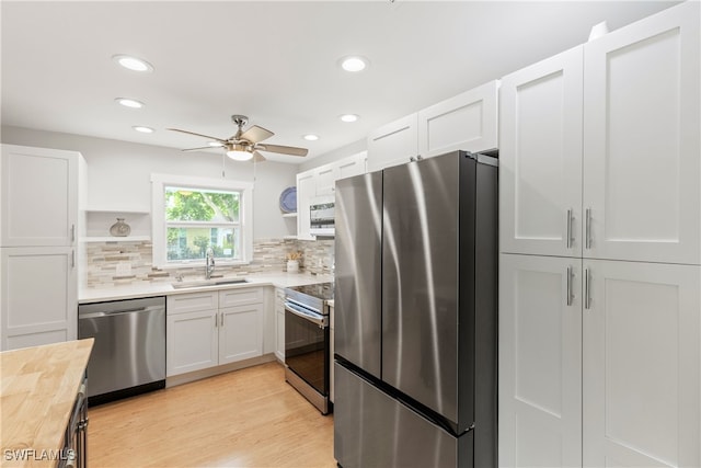 kitchen featuring appliances with stainless steel finishes, light hardwood / wood-style floors, white cabinetry, sink, and ceiling fan