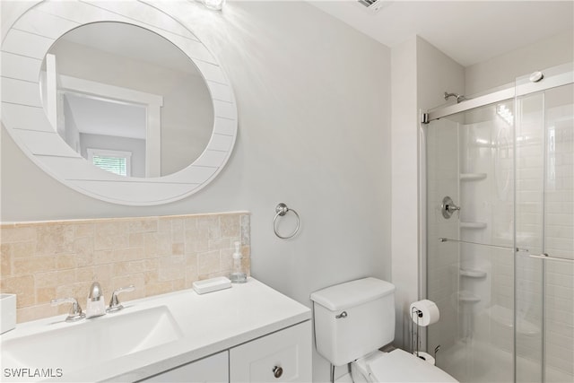 bathroom featuring vanity, toilet, a shower with shower door, and tasteful backsplash