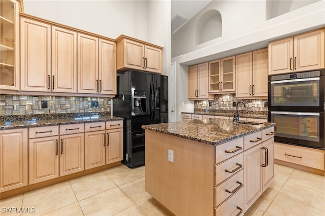 kitchen featuring black appliances, high vaulted ceiling, dark stone countertops, a center island with sink, and backsplash