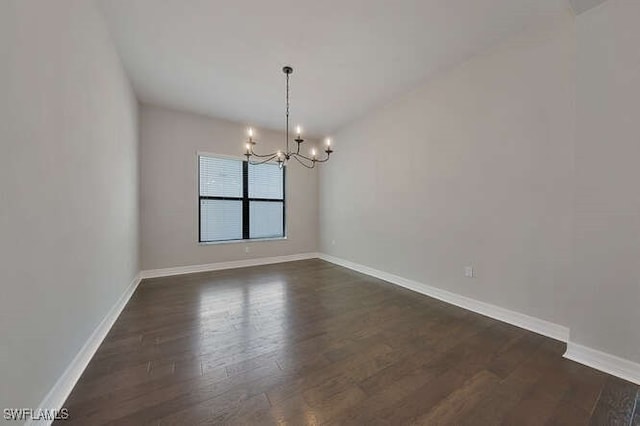 spare room with dark hardwood / wood-style flooring and an inviting chandelier