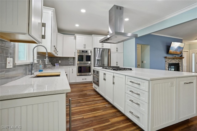 kitchen with white cabinetry, dark wood-type flooring, stainless steel appliances, island exhaust hood, and a stone fireplace