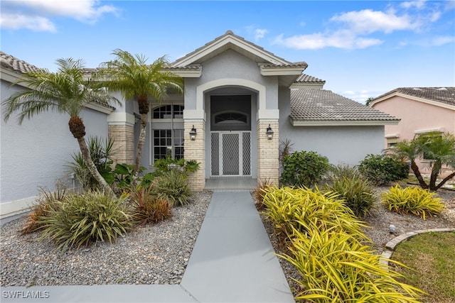 entrance to property with brick siding, a tile roof, and stucco siding