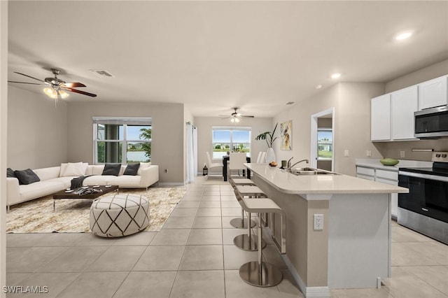 kitchen with white cabinets, stainless steel appliances, sink, a kitchen island with sink, and light tile patterned flooring