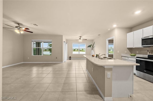 kitchen with light tile patterned floors, appliances with stainless steel finishes, a kitchen island with sink, white cabinets, and sink