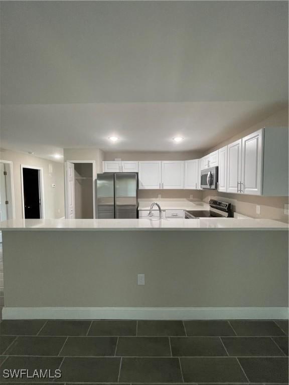 kitchen with sink, white cabinetry, appliances with stainless steel finishes, kitchen peninsula, and dark tile patterned floors