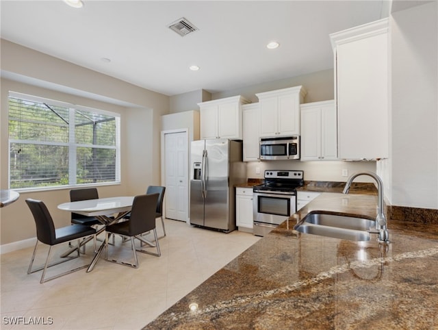 kitchen featuring dark stone counters, light tile patterned floors, sink, appliances with stainless steel finishes, and white cabinets