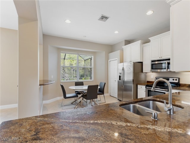 kitchen featuring dark stone counters, light tile patterned flooring, sink, appliances with stainless steel finishes, and white cabinets