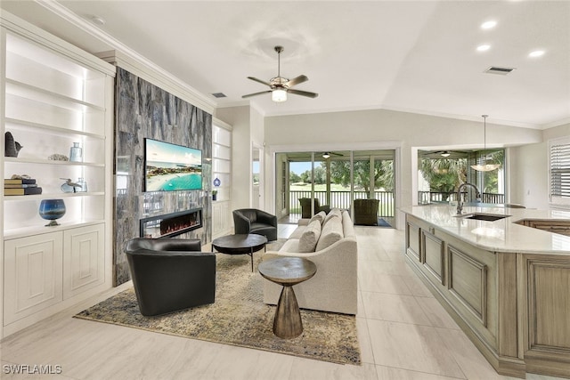 living room with built in shelves, ornamental molding, a tiled fireplace, ceiling fan, and vaulted ceiling