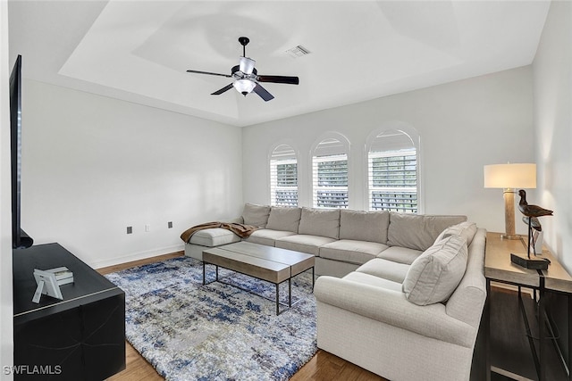 living room featuring a tray ceiling, wood finished floors, a ceiling fan, and visible vents